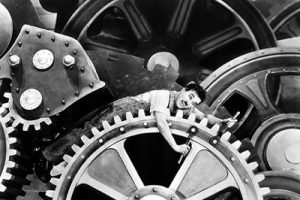 A picture of Charlie Chaplin wedged between GIANT gears while working on one of the gears pins